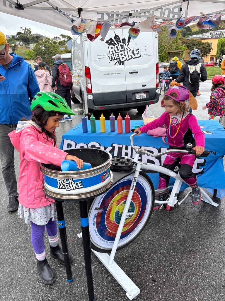Children playing with a bike-themed game at an outdoor event with 'Rock the Bike' branding.